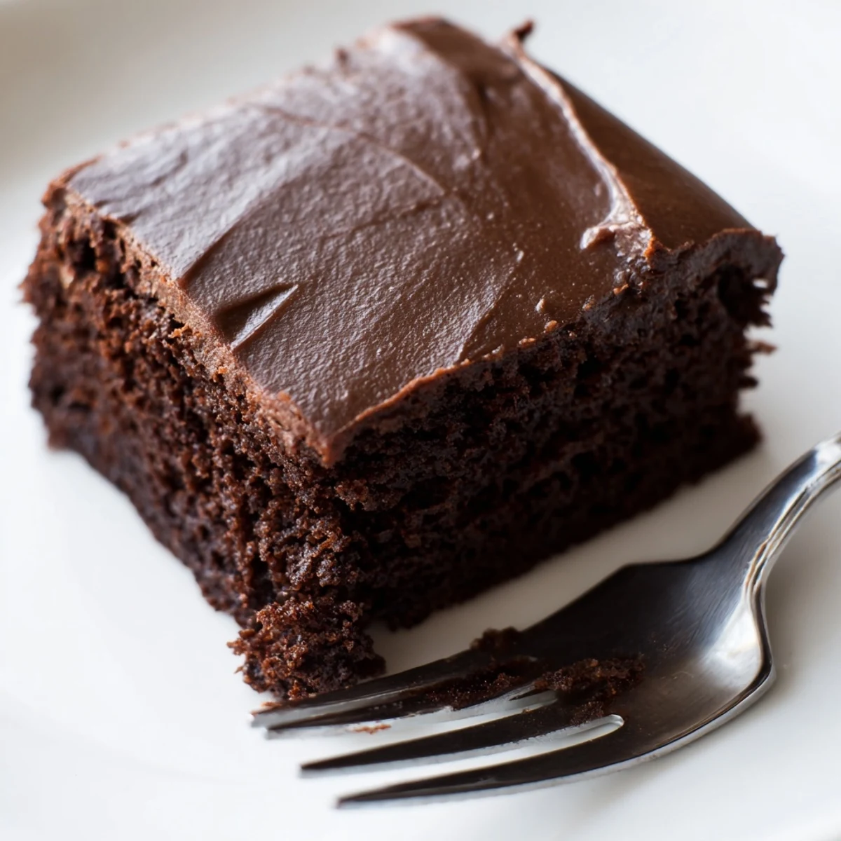 Moist Chocolate Brownies with Fudge Frosting topped with a velvety chocolate ganache, ready to serve on a white plate.