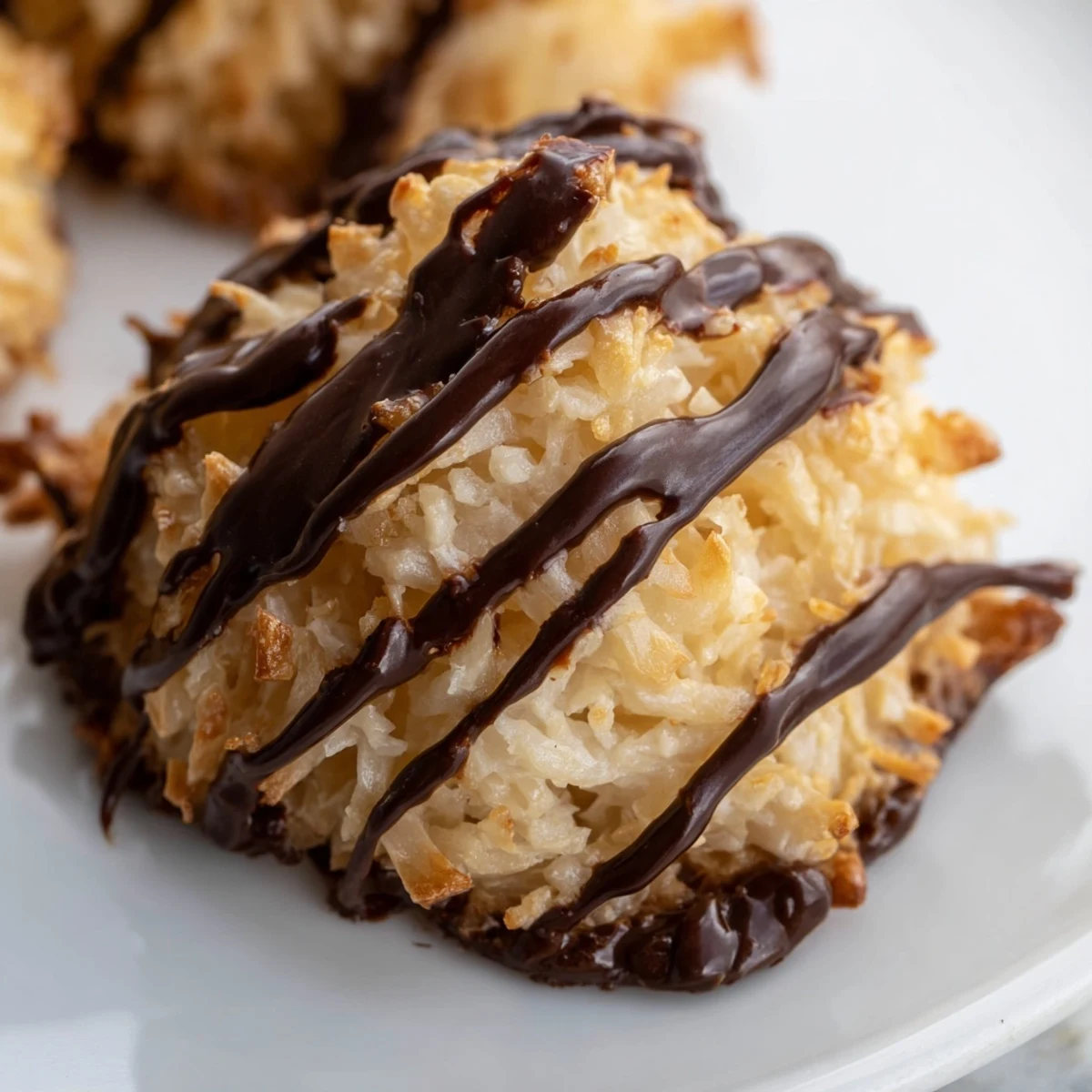Freshly baked gluten-free coconut macaroons dipped in dark chocolate, placed on parchment paper.