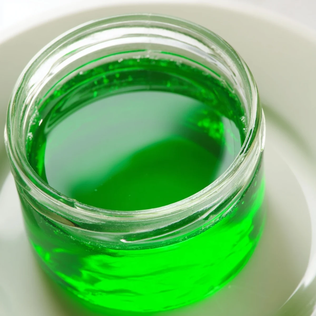 A glass bottle of homemade Peppermint Schnapps syrup sits beside fresh mint leaves.