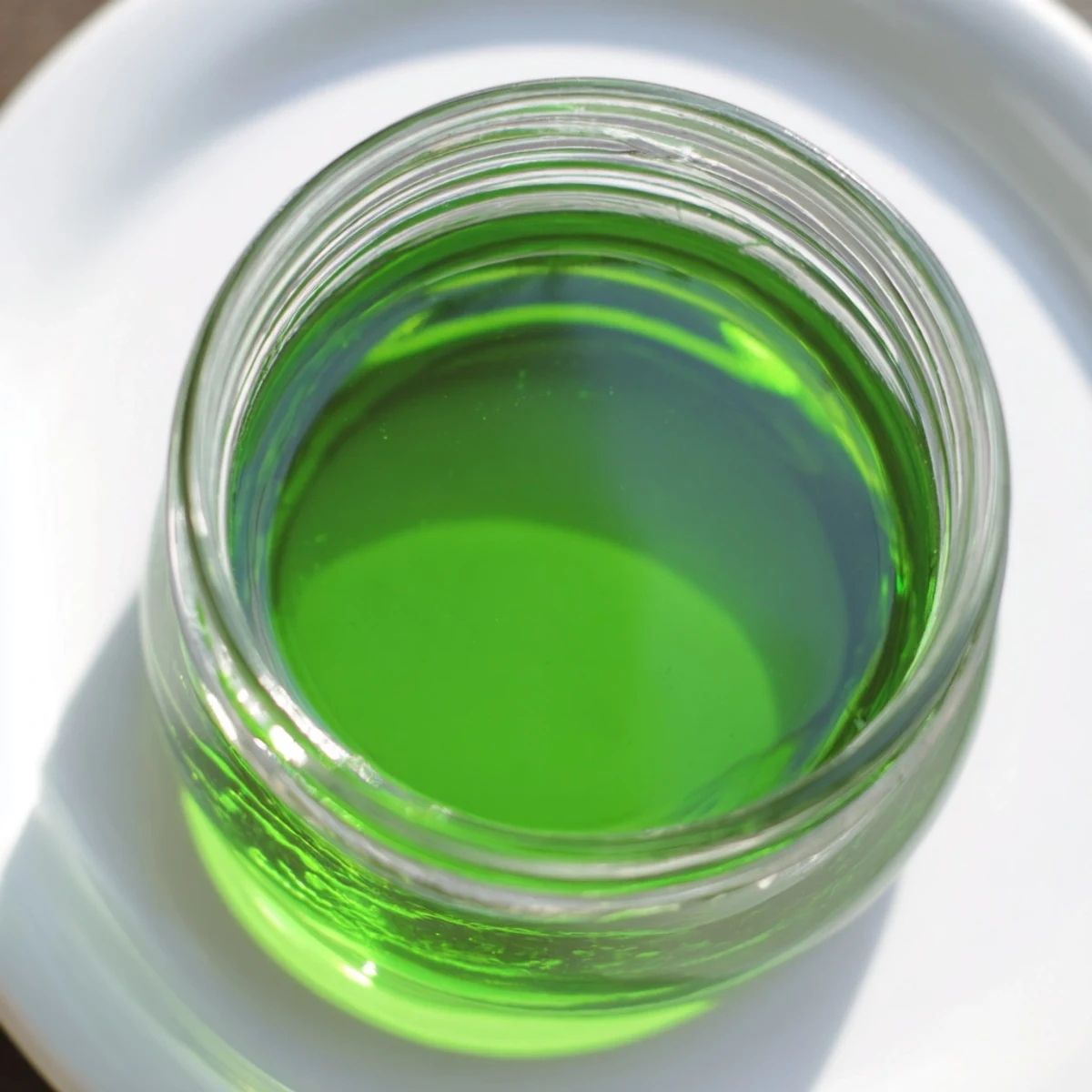 Clear Peppermint Schnapps syrup is poured into a glass over ice cubes.