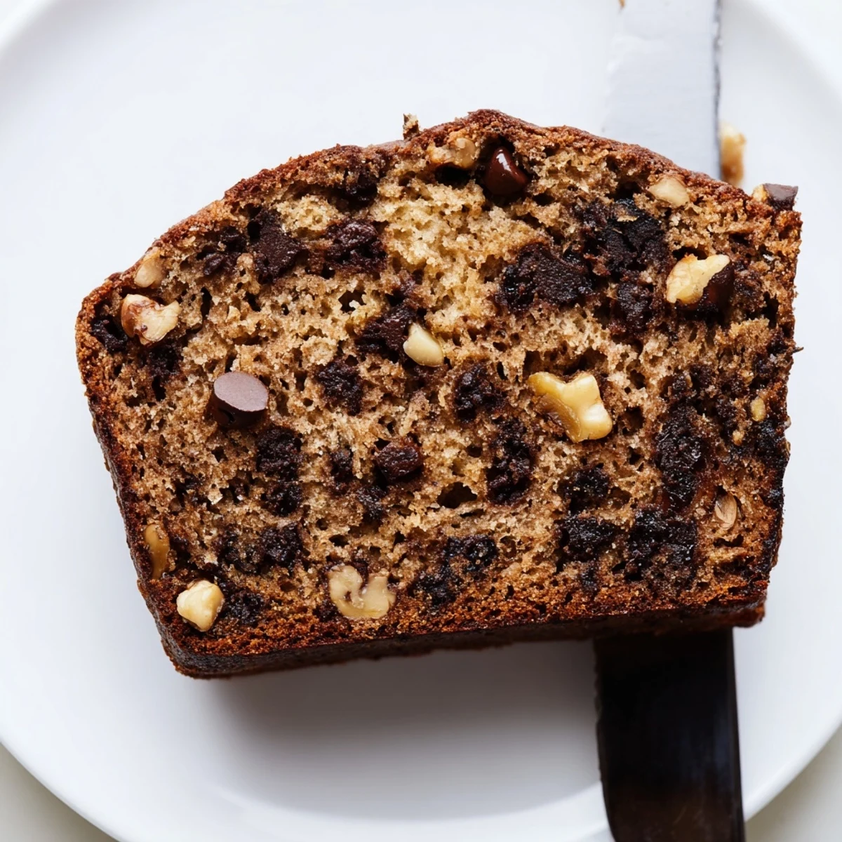 A sliced loaf of Chocolate Banana Bread revealing a moist, dark crumb and melted chocolate chunks.