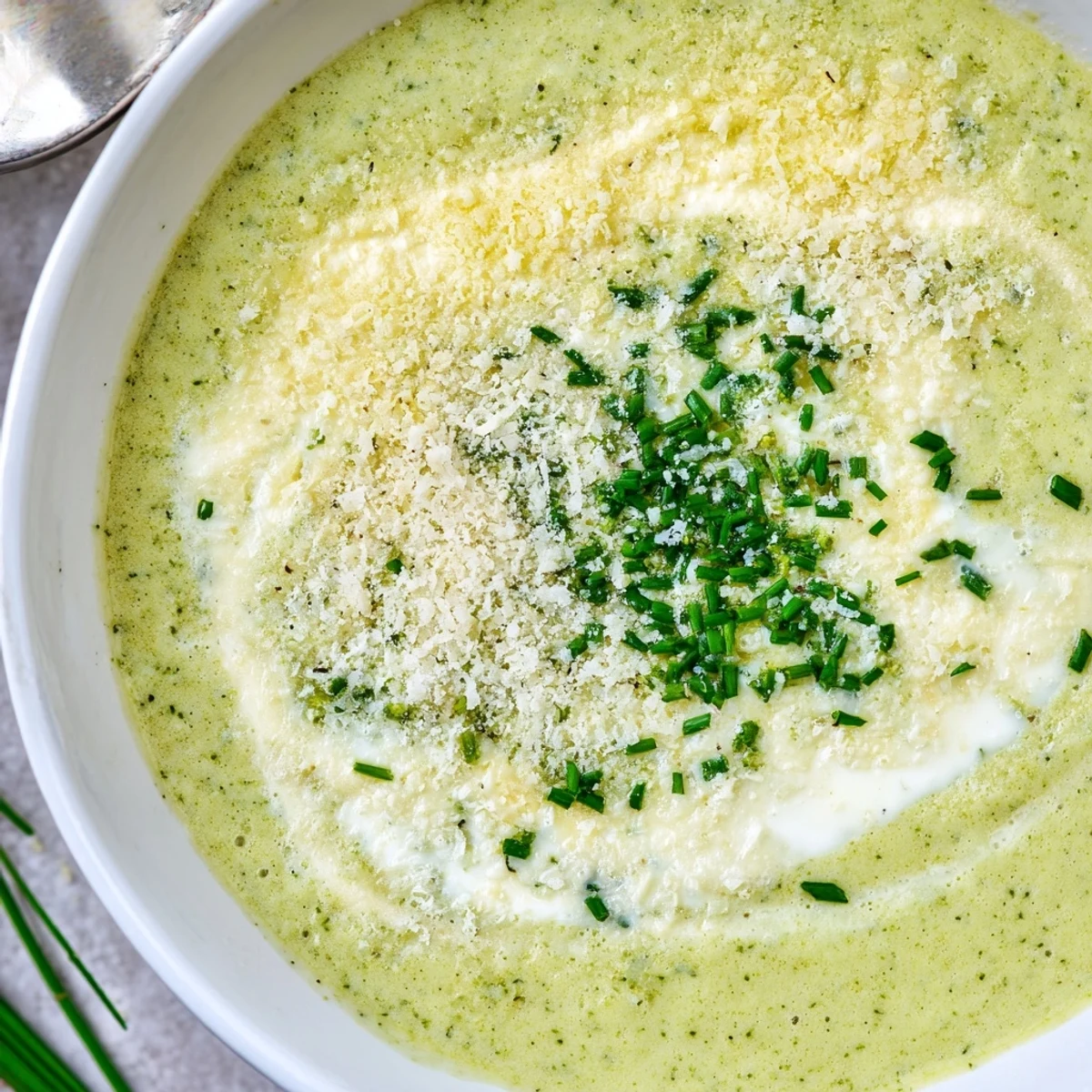 A spoon lifting velvety Creamy Broccoli Soup, served beside crusty bread for dipping.