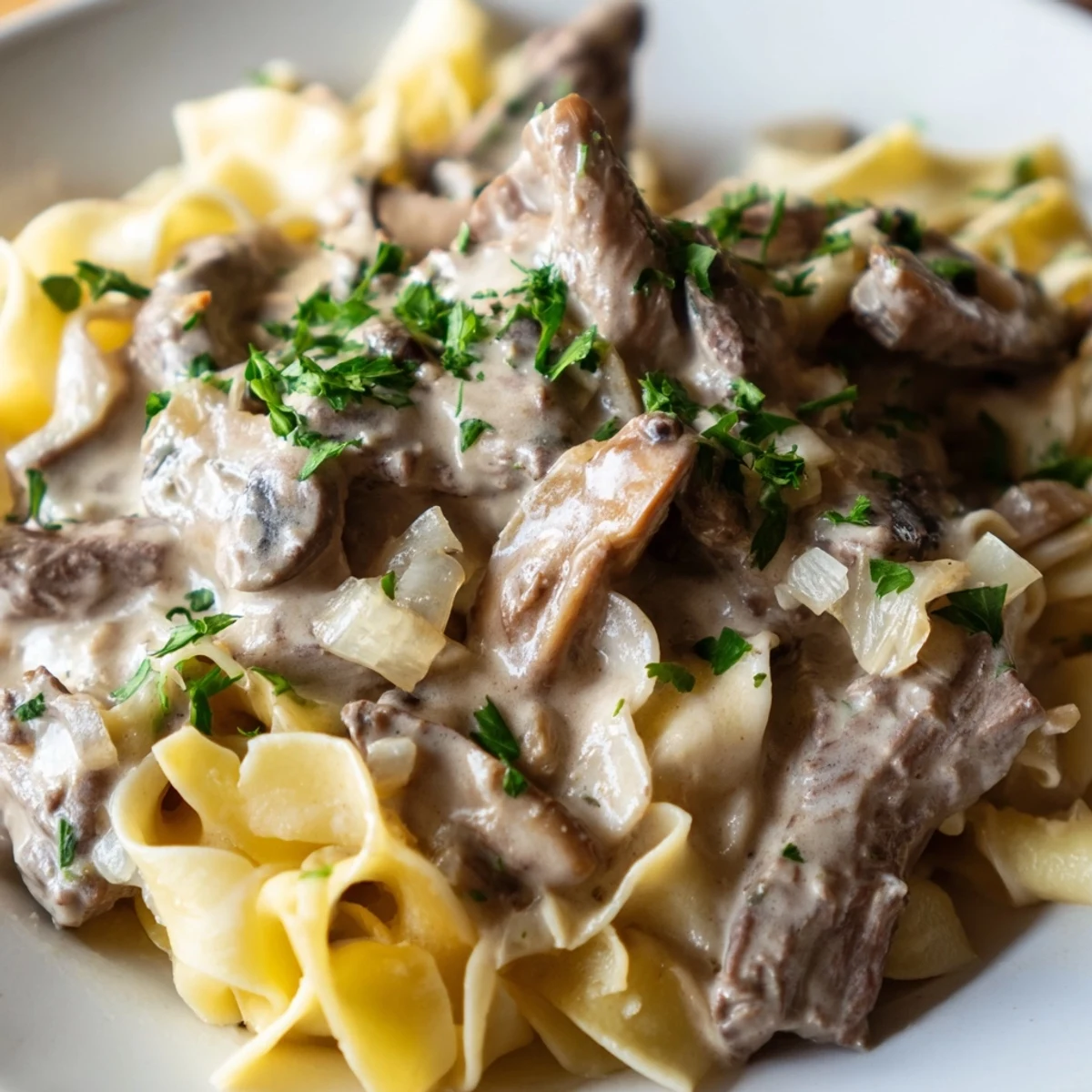 Creamy Beef Stroganoff over Egg Noodles garnished with fresh parsley in a skillet.
