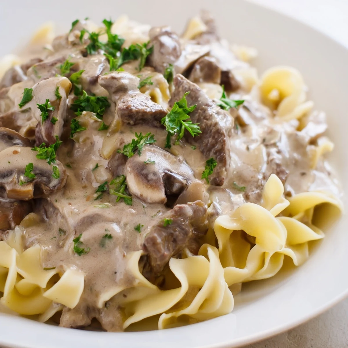 Savory Beef Stroganoff over Egg Noodles served on a plate with a fork.