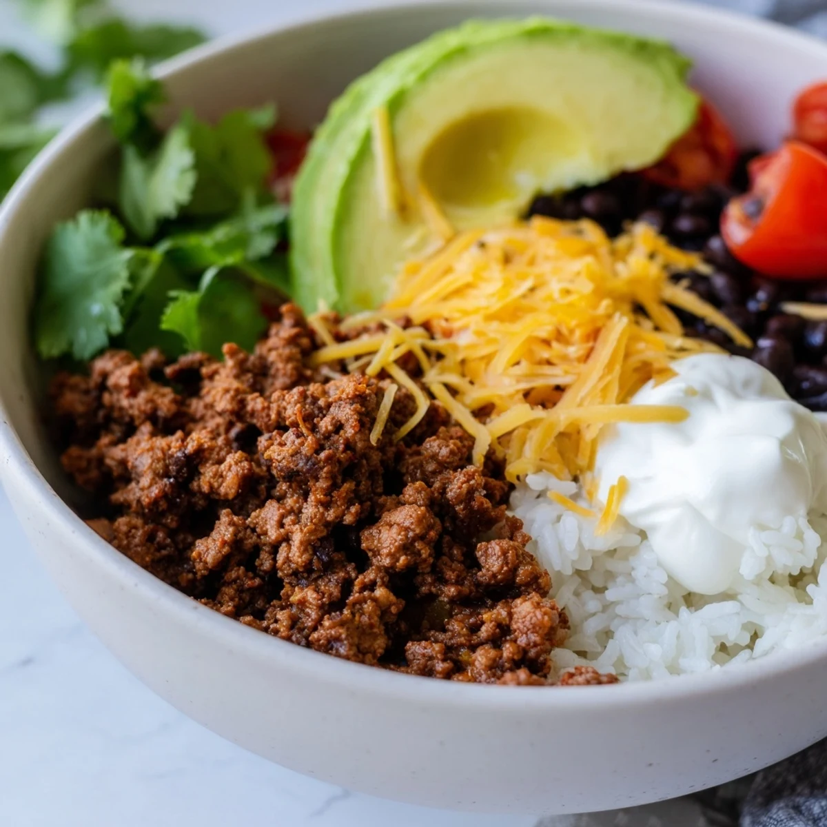 A hearty serving of Beef Burrito Bowl with Rice and Beans featuring black beans, crisp lettuce, juicy tomatoes, and creamy avocado slices topped with sour cream.