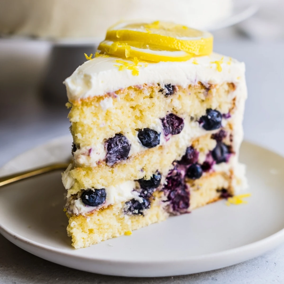 A slice of Lemon Blueberry Cake with Cream Cheese Frosting shows juicy berries in fluffy cake and rich white frosting.