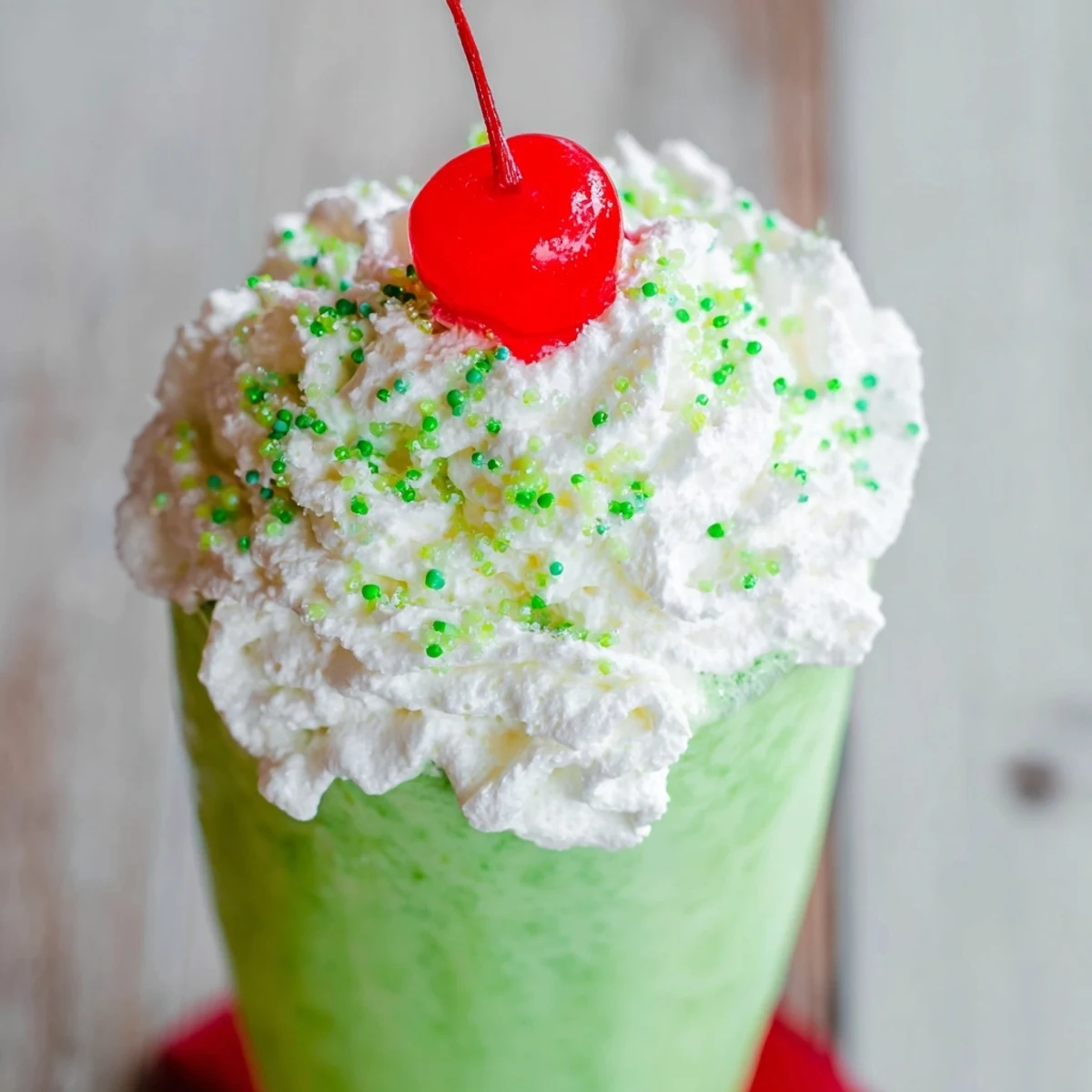 Two tall glasses of Shamrock Shake with Whipped Cream sit beside fresh mint leaves and a festive green sprinkle garnish.