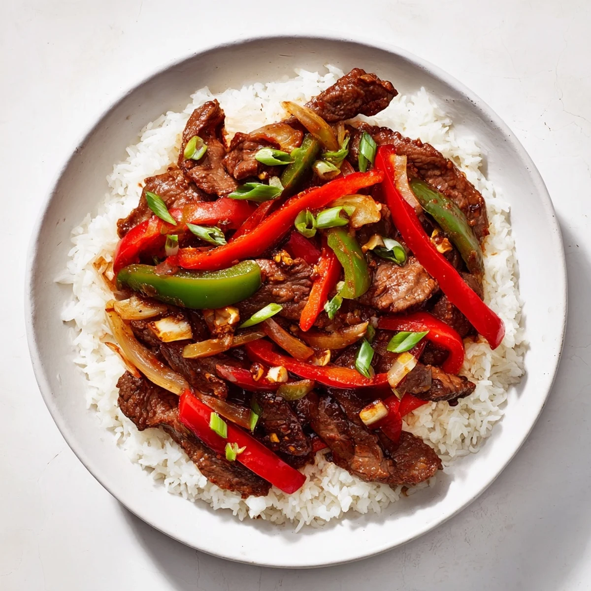 Spicy beef stir-fry is served over fluffy jasmine rice, with colorful peppers and onions.