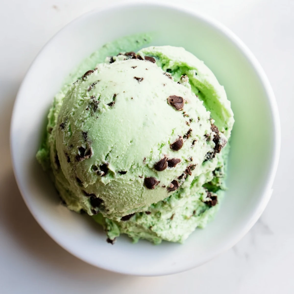 Homemade mint chip ice cream with dark chocolate pieces in a chilled dish.