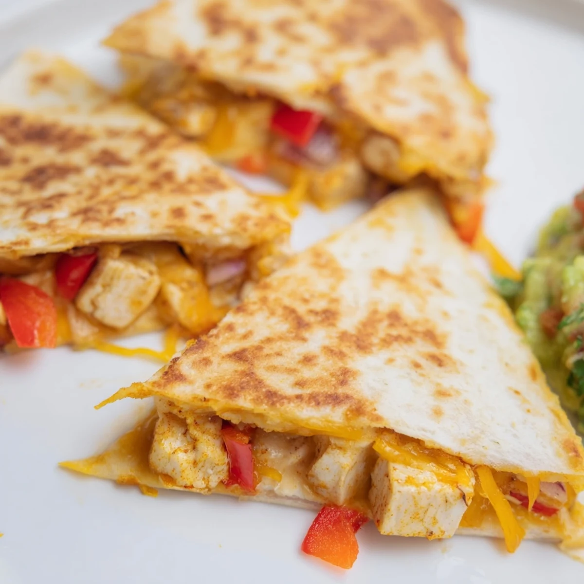 Golden-brown Championship Chicken Quesadillas with Guacamole are sliced into wedges on a plate.
