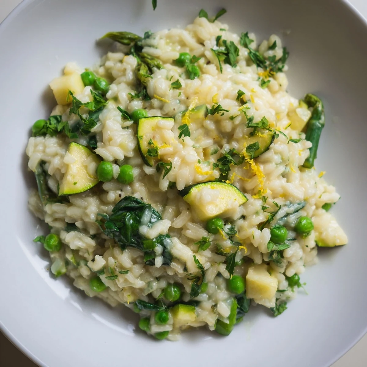 Vibrant Spring Vegetable Risotto with lemon zest, creamy rice, peas, asparagus, and zucchini in a pan from above.