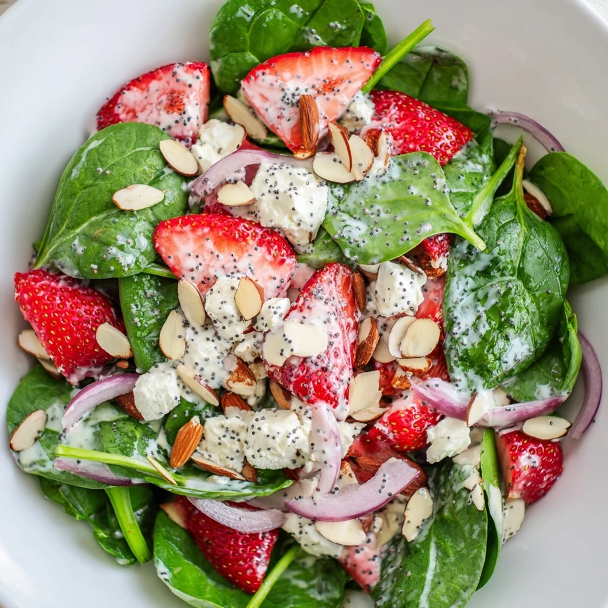 Fresh baby spinach and sliced strawberries topped with crumbled feta and toasted almonds in a vibrant salad bowl.