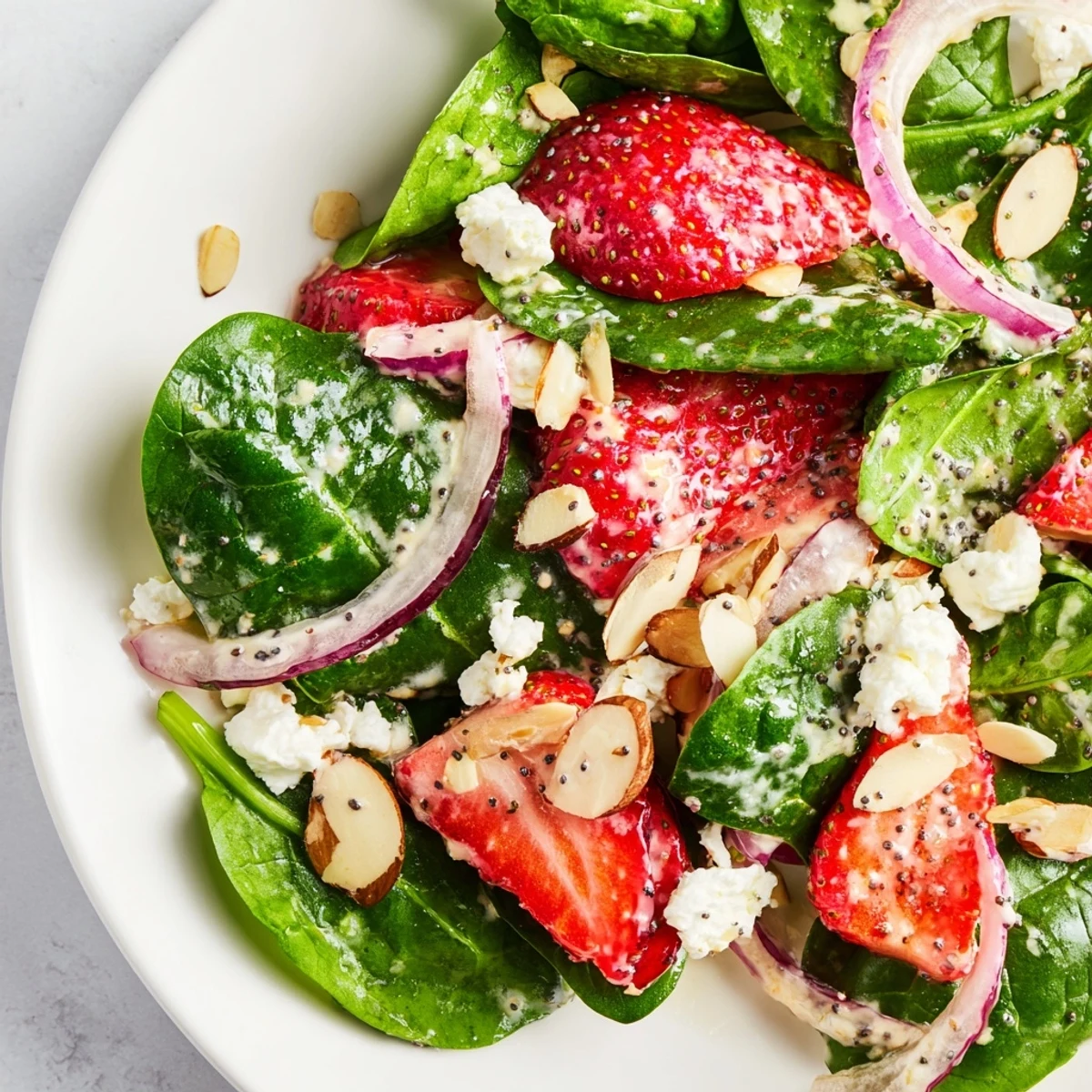 Overhead view of a serving plate showcasing Strawberry Spinach Salad with Poppy Seed Dressing, red onion, and nuts.