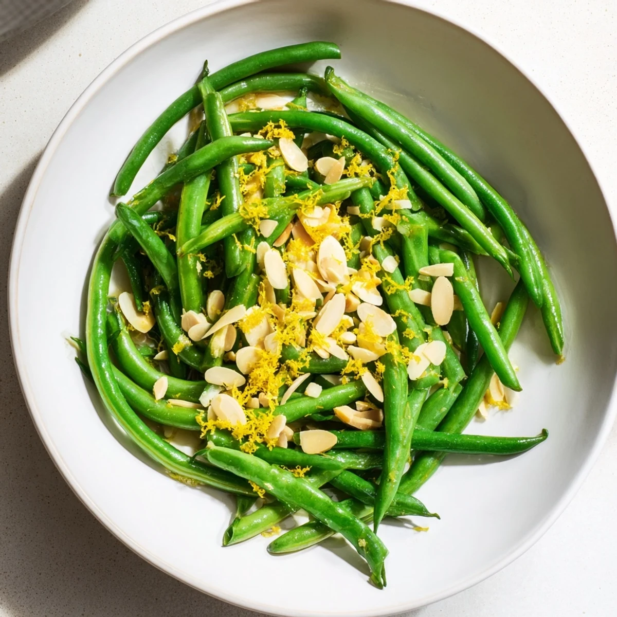 Freshly blanched green beans with toasted almonds and lemon garnish are served warm alongside roasted chicken.