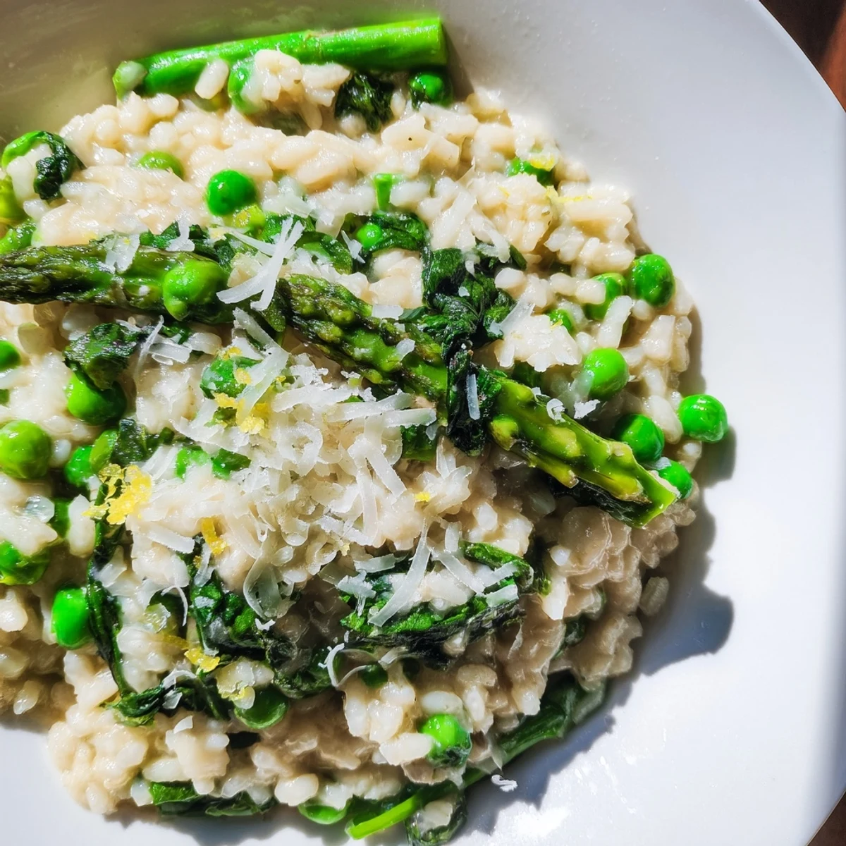 A close-up of Spring Vegetable Risotto with Lemon Zest highlighting a wooden spoon and vibrant greens.