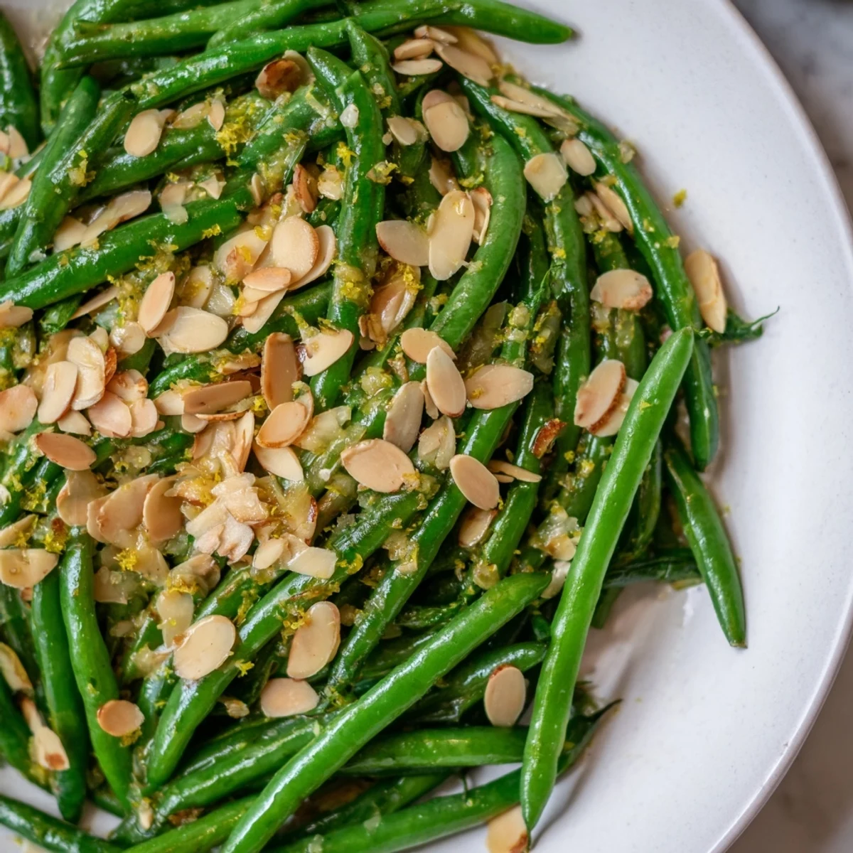 Green Beans with Toasted Almonds and Lemon on a white plate, garnished with lemon zest and fresh herbs.  