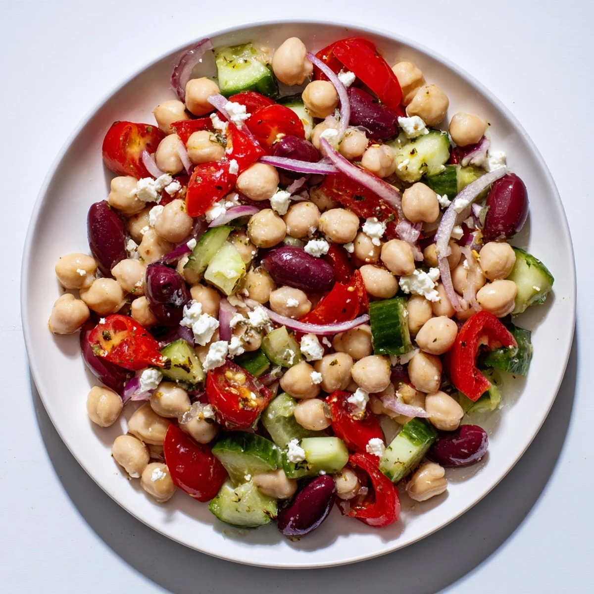 Colorful Mediterranean Dense Bean Salad in a white bowl, with chickpeas, cucumbers, tomatoes, and crumbled feta.