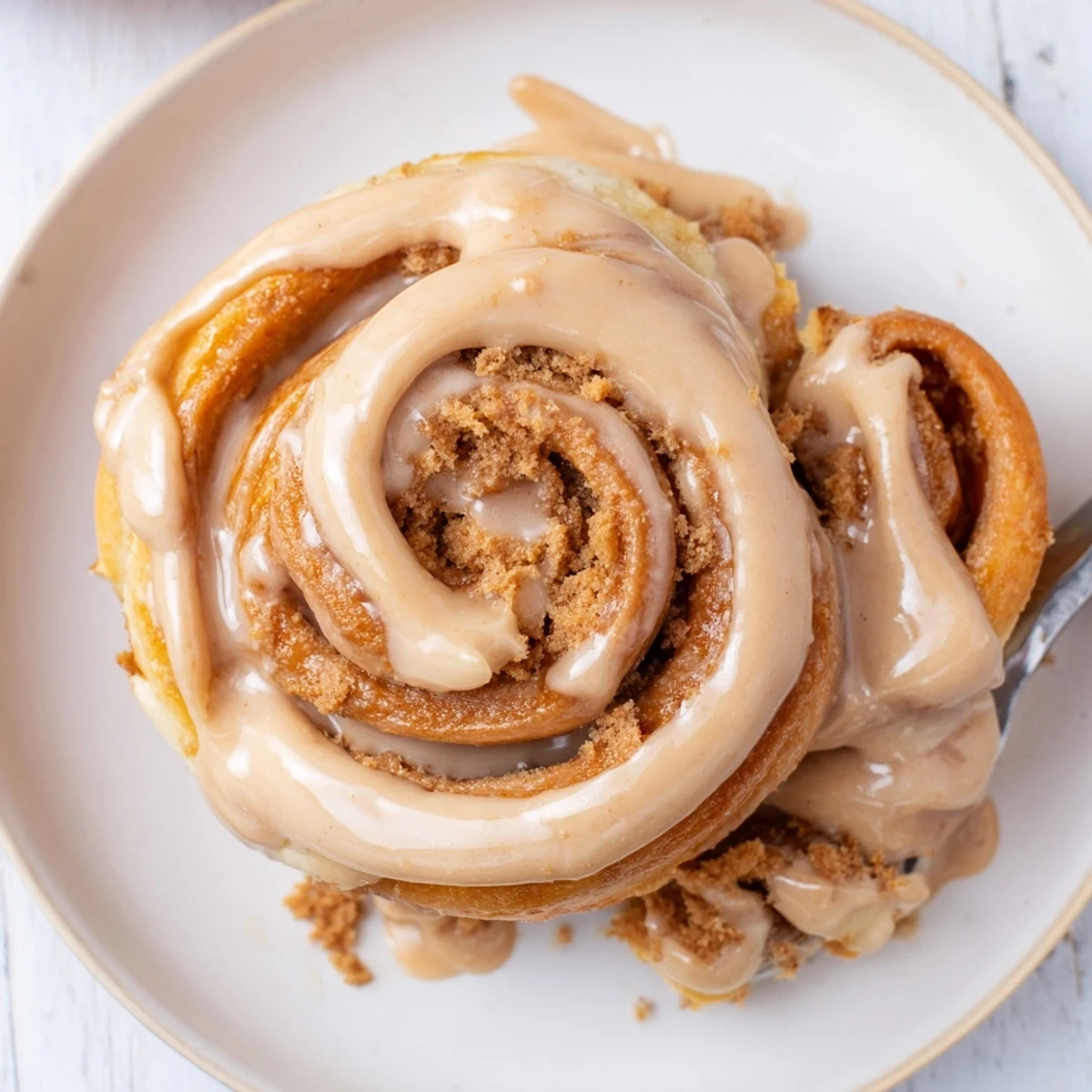 Freshly baked Soft and Gooey Biscoff Cinnamon Rolls on a white plate with a glass of milk, showing the warm caramel swirl and drizzle.