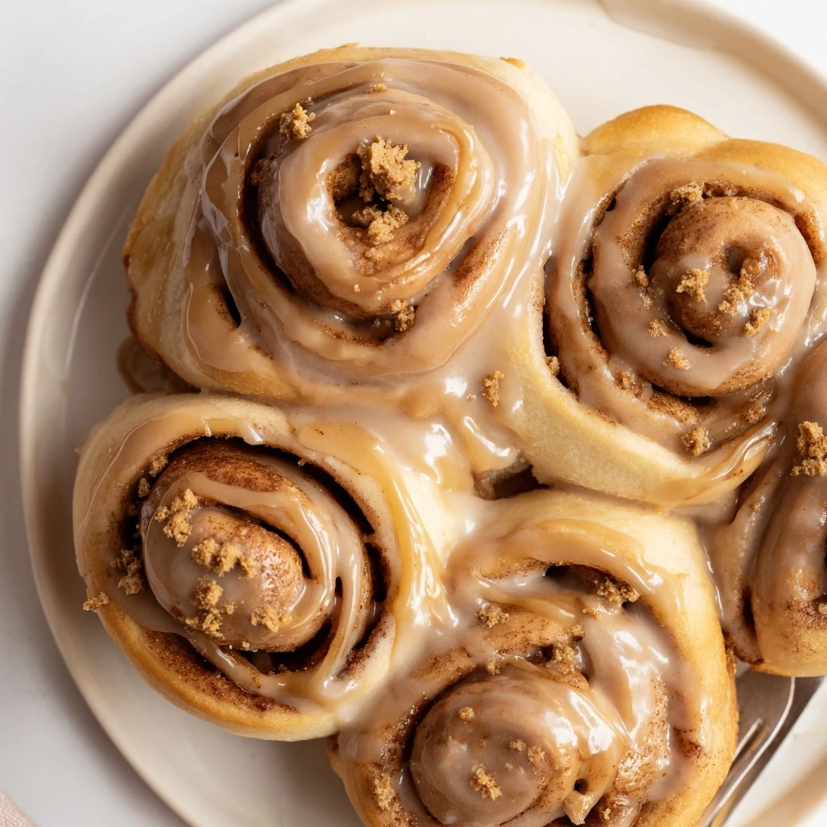 Close-up of Soft and Gooey Biscoff Cinnamon Rolls on a marble counter, highlighting the fluffy texture and rich Biscoff glaze drizzle.