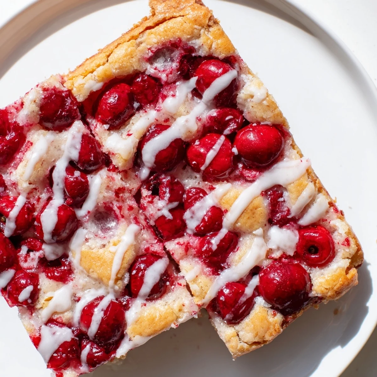 A slice of Easy Cherry Pie Bars on a white plate, drizzled with sweet vanilla glaze and a scoop of vanilla ice cream.