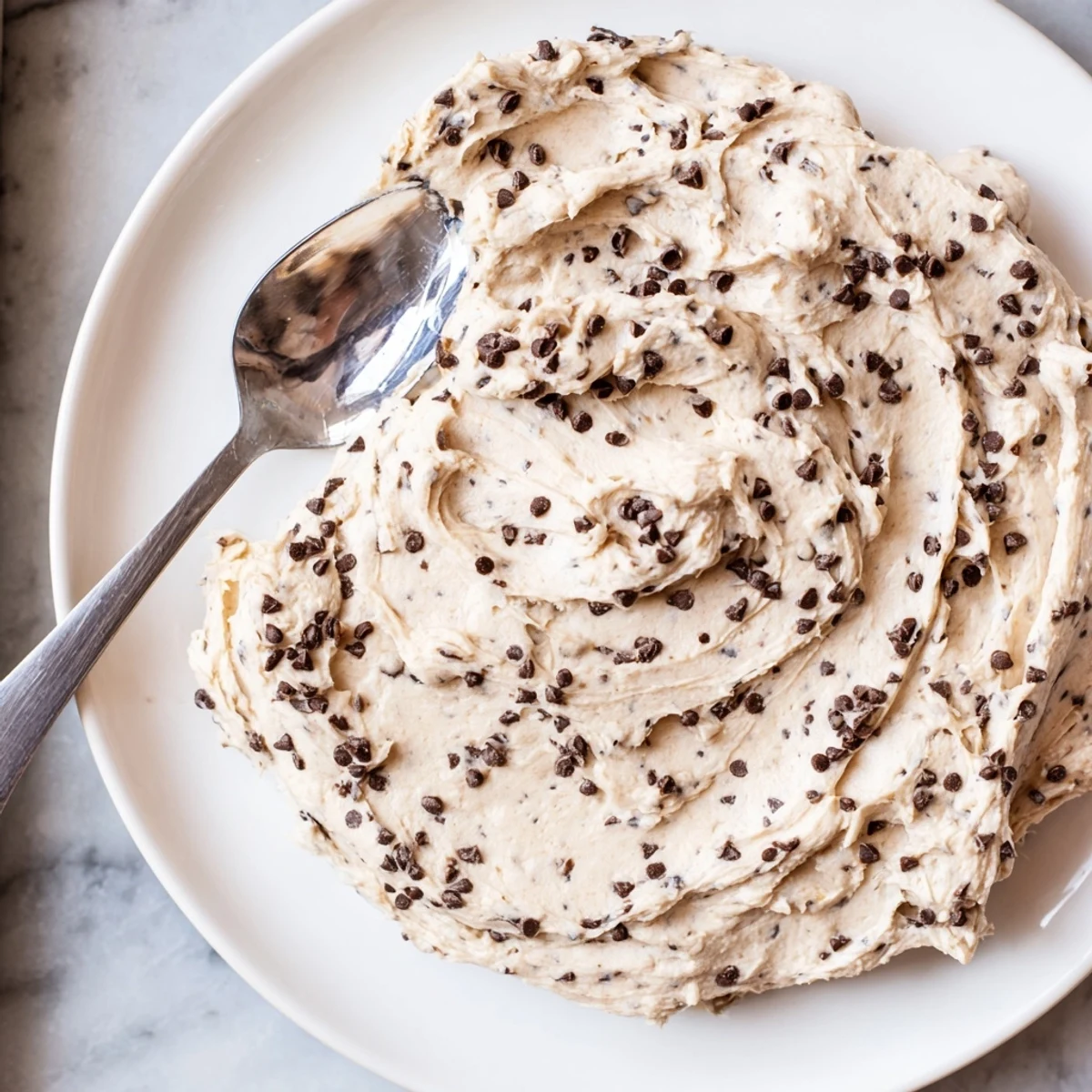 Thick, sweet Cookie Dough Frosting with a spoonful showing rich brown sugar, butter, and glossy chocolate chips perfect for a 9-inch cake.