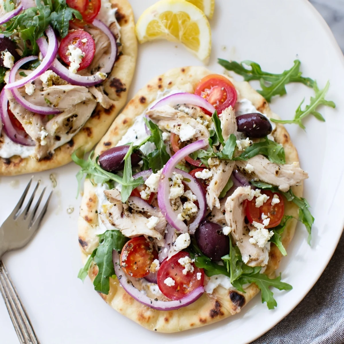 Golden-brown slices of lemon-herb chicken rest on a Zesty Lemon Herb Chicken Flatbread With Creamy Feta, topped with vibrant cherry tomatoes and red onion.