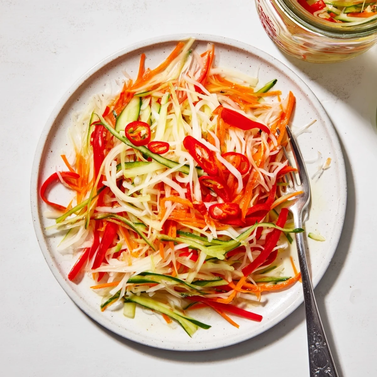 A jar of Vietnamese Vegetable Pickle Medley filled with bright pink radish and orange carrot ribbons, glistening in sweet tangy brine.