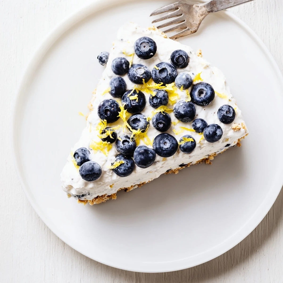 Creamy no bake lemon blueberry cake slice showing purple blueberries swirled through light lemon filling on cracker base