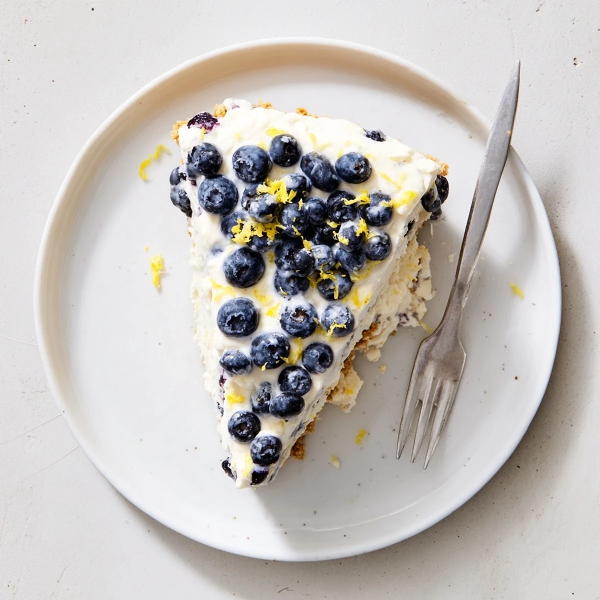 No bake lemon blueberry cream cake topped with fresh blueberries and lemon zest on a graham cracker crust