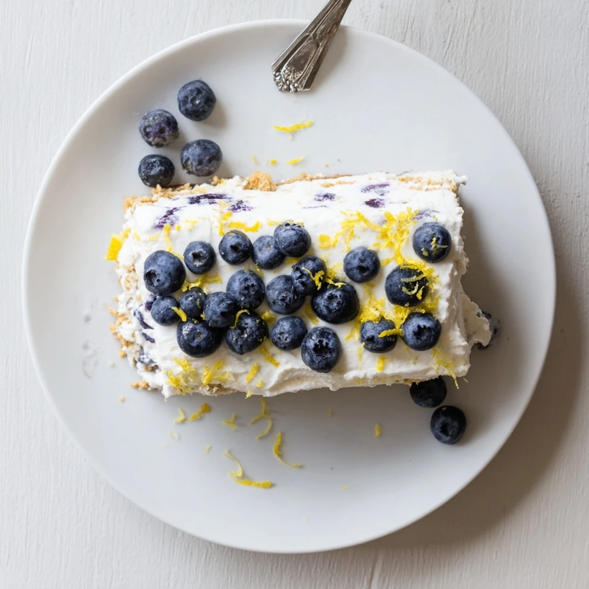 Sliced no bake lemon blueberry cream cake garnished with whipped cream and fresh berries on white serving plate