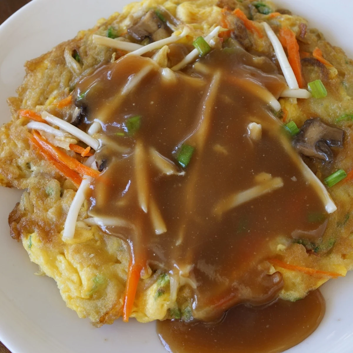 Golden crispy Egg Foo Young patties topped with rich savory brown gravy on white plate