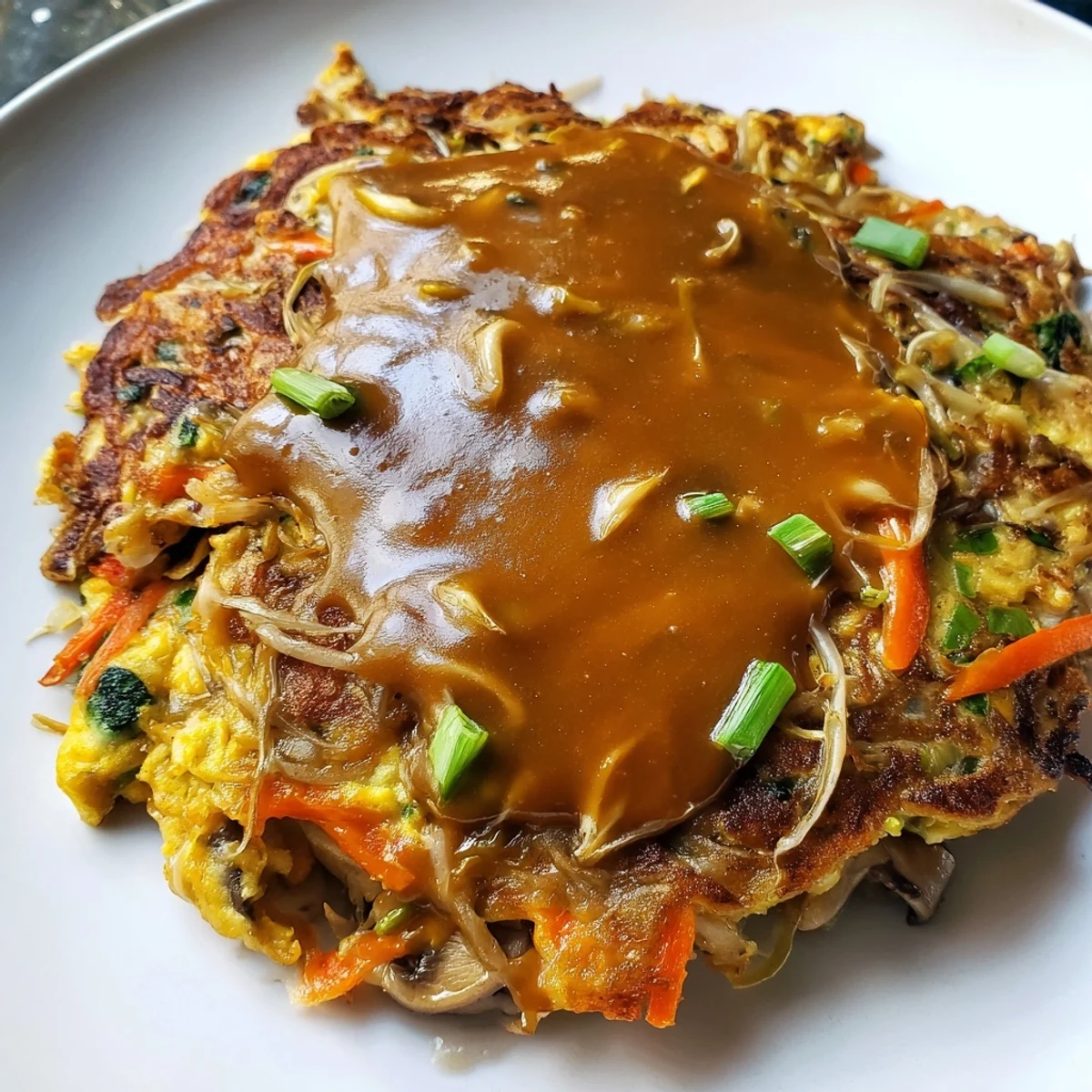Fluffy Chinese-style Egg Foo Young omelet packed with colorful vegetables and drizzled with sauce