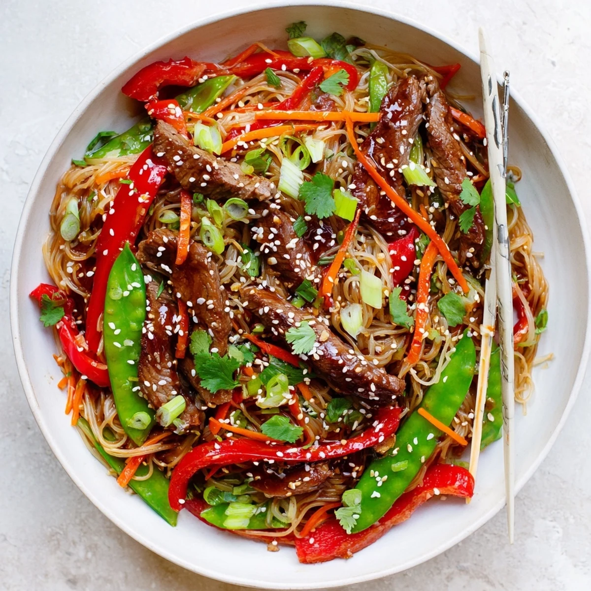 Sizzling plate of sticky beef noodles loaded with marinated beef, julienned carrots, and fresh cilantro garnish over saucy noodles