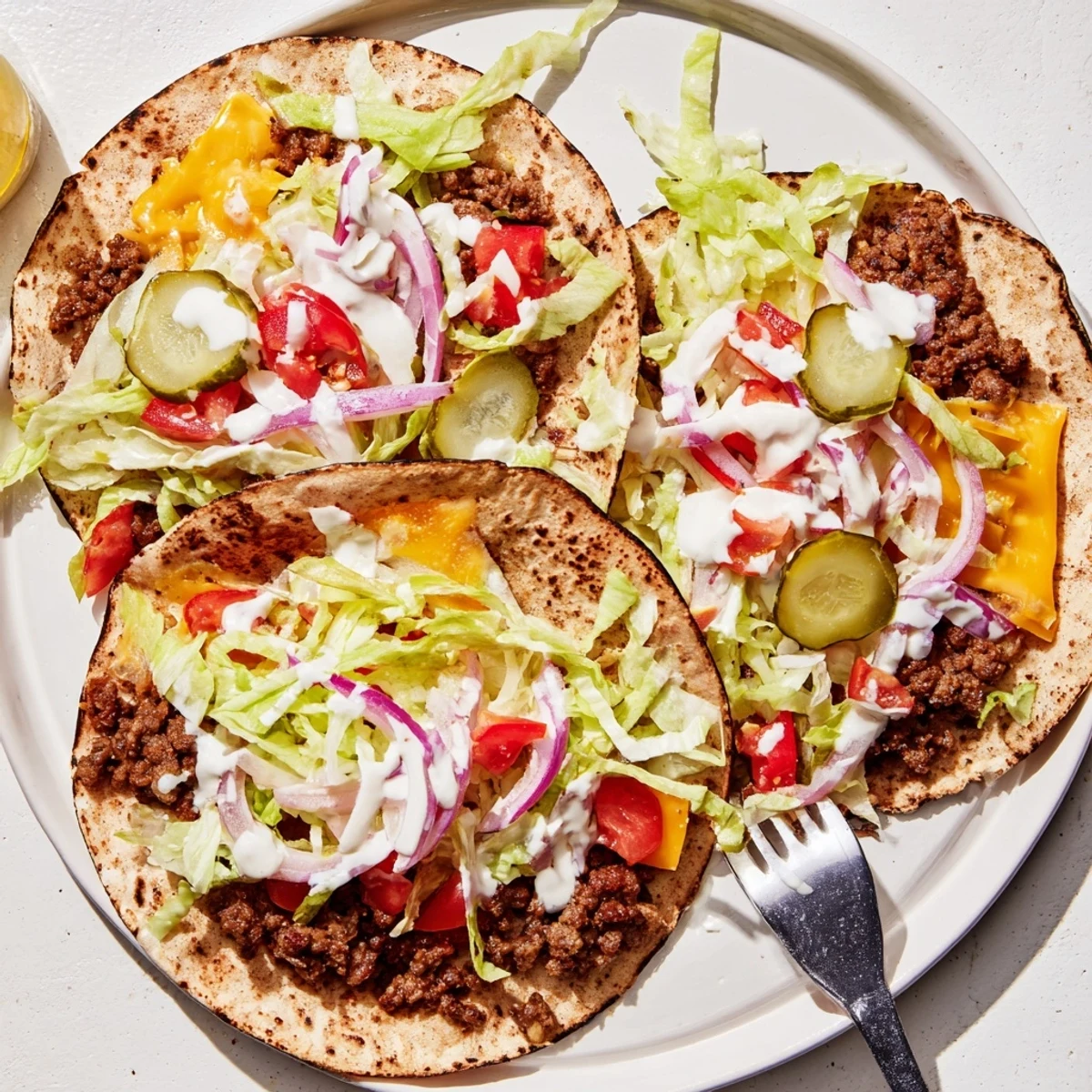 Juicy beef smash burger tacos piled high with diced tomatoes, red onion, and pickle chips on golden toasted tortillas