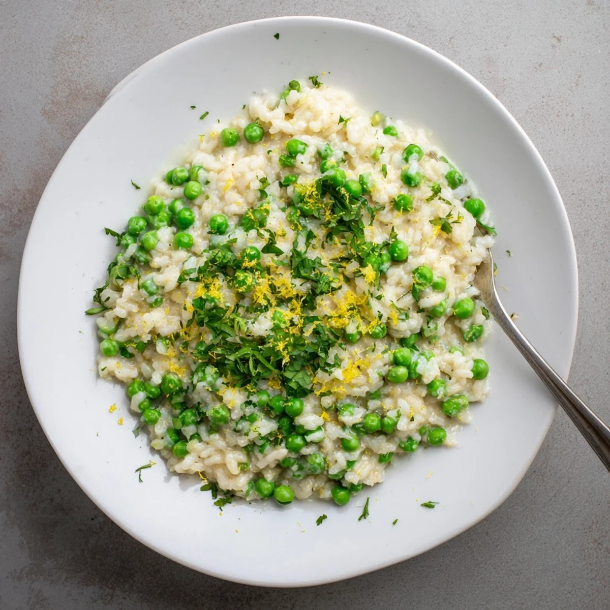 Golden Arborio rice simmered with sweet peas and fresh mint in a white shallow bowl