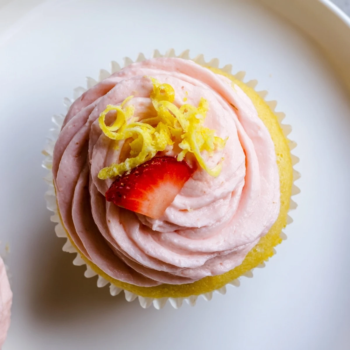 Freshly baked lemon cupcakes topped with naturally pink strawberry buttercream on white plate