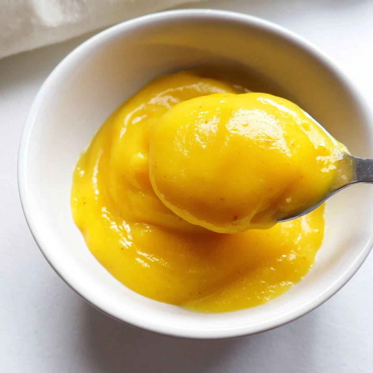 Golden easy vegan mango curd spooned into a glass jar with fresh mango chunks nearby