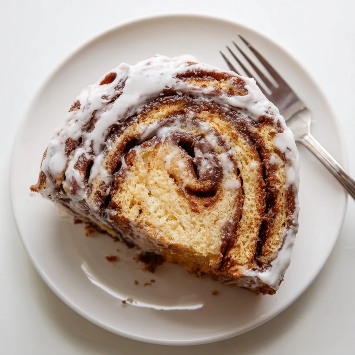 Warm swirled cinnamon roll cake slice showing marbled cinnamon sugar layers topped with silky icing
