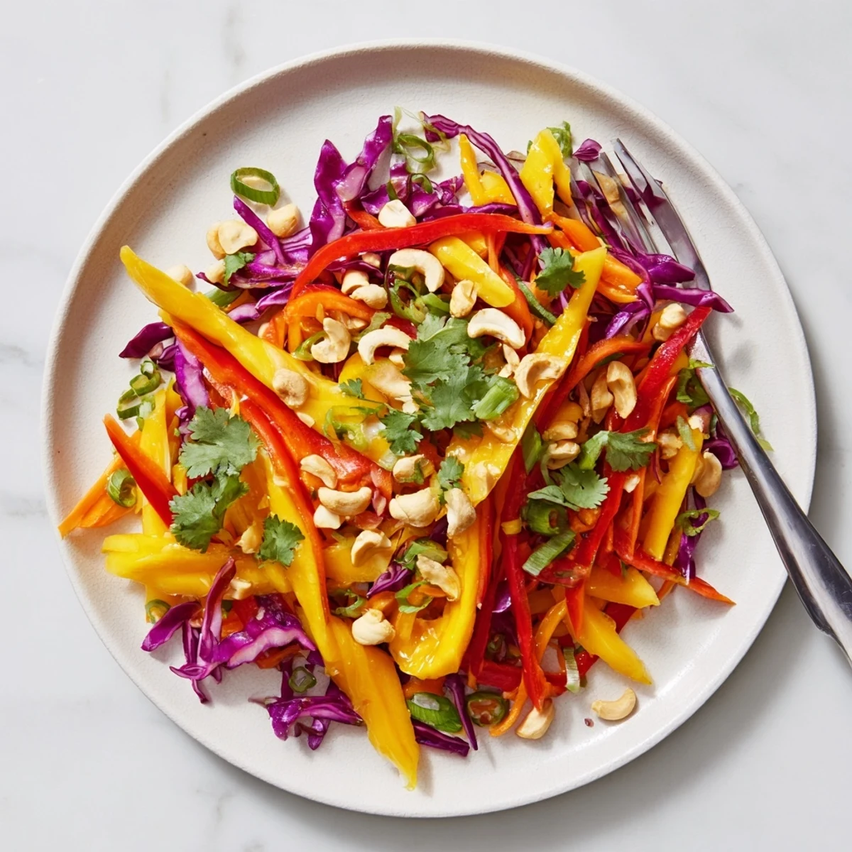 Fresh mango slaw topped with toasted cashews and green onions in white bowl
