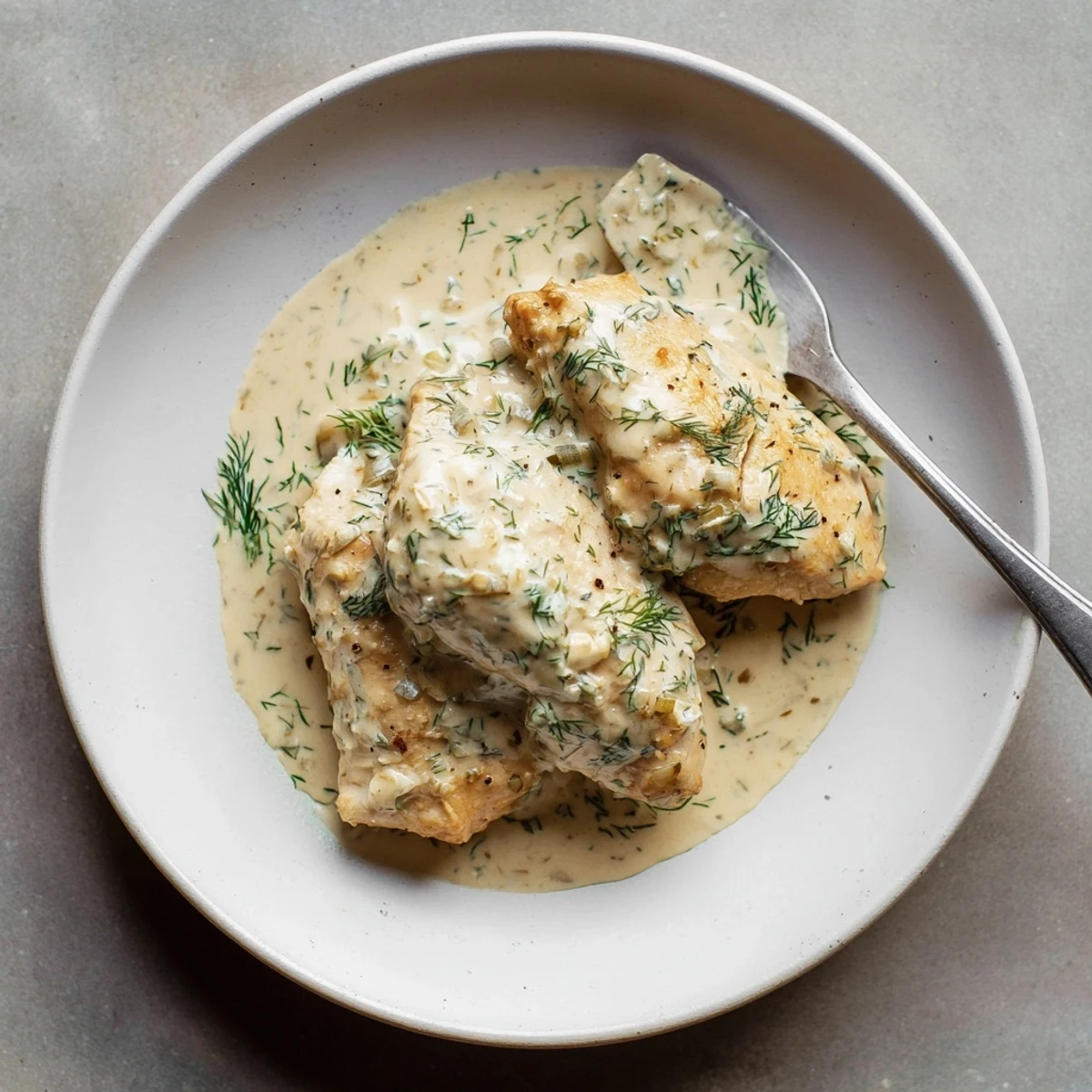 Golden creamy dill chicken breasts in rich white sauce garnished with fresh green herbs