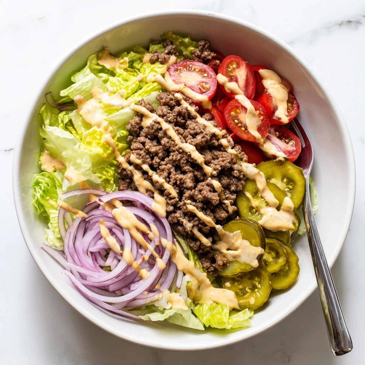 Deconstructed burger bowl with ground beef, crisp lettuce, diced tomatoes, and drizzled burger sauce.