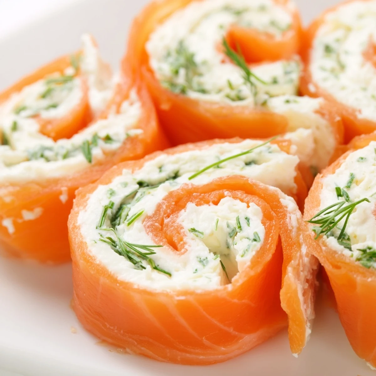 Close-up of spiral sliced smoked salmon roll ups on white serving plate with herbs