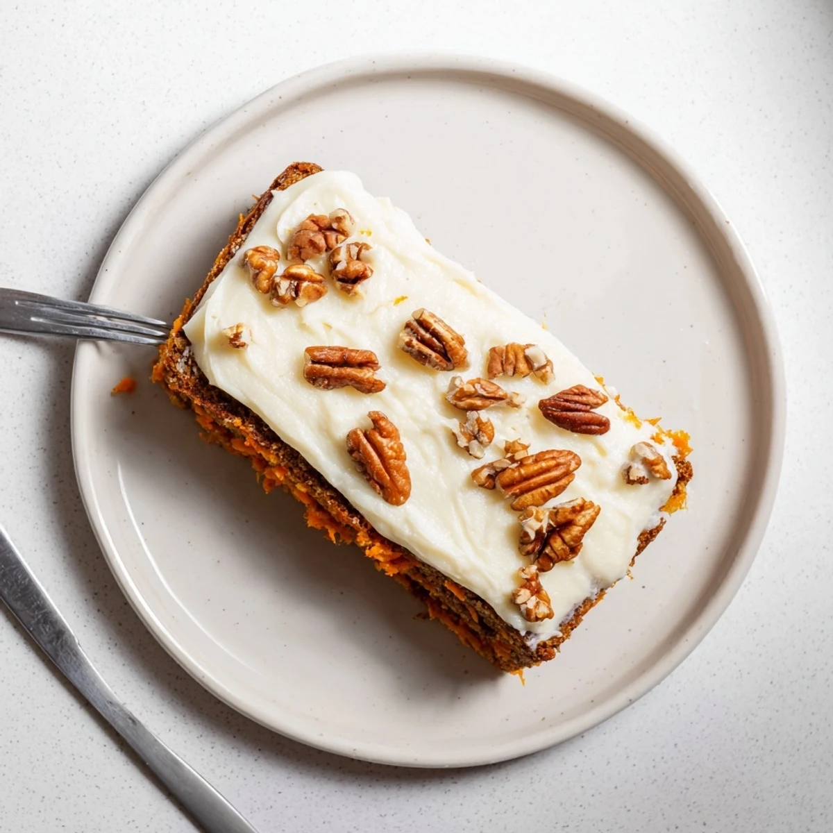Homemade carrot cake bars displaying rich texture beneath luscious cream cheese frosting layer