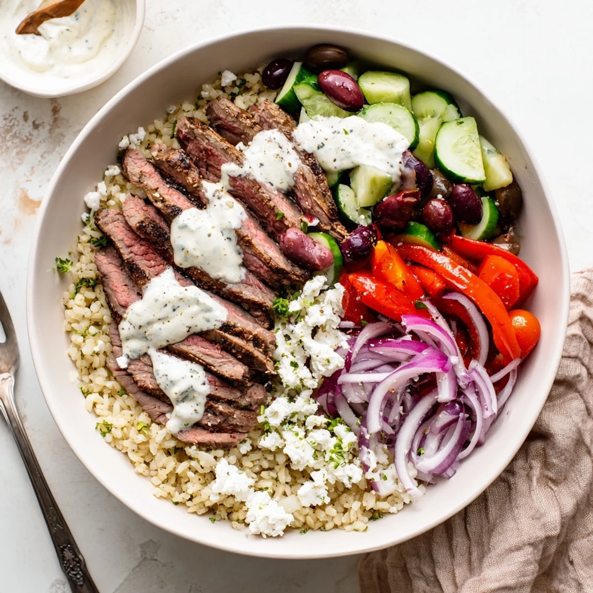 Sliced grilled steak arranged in a colorful bowl with cherry tomatoes, cucumber, olives, and crumbled feta cheese
