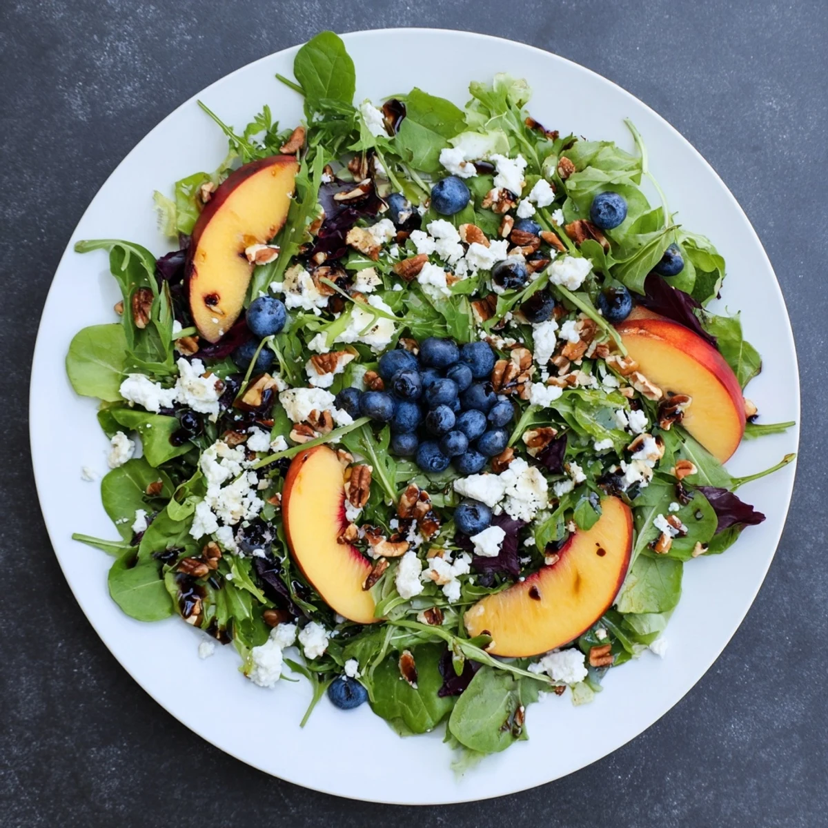 Colorful blueberry peach feta salad topped with toasted pecans and sweet honey balsamic vinaigrette