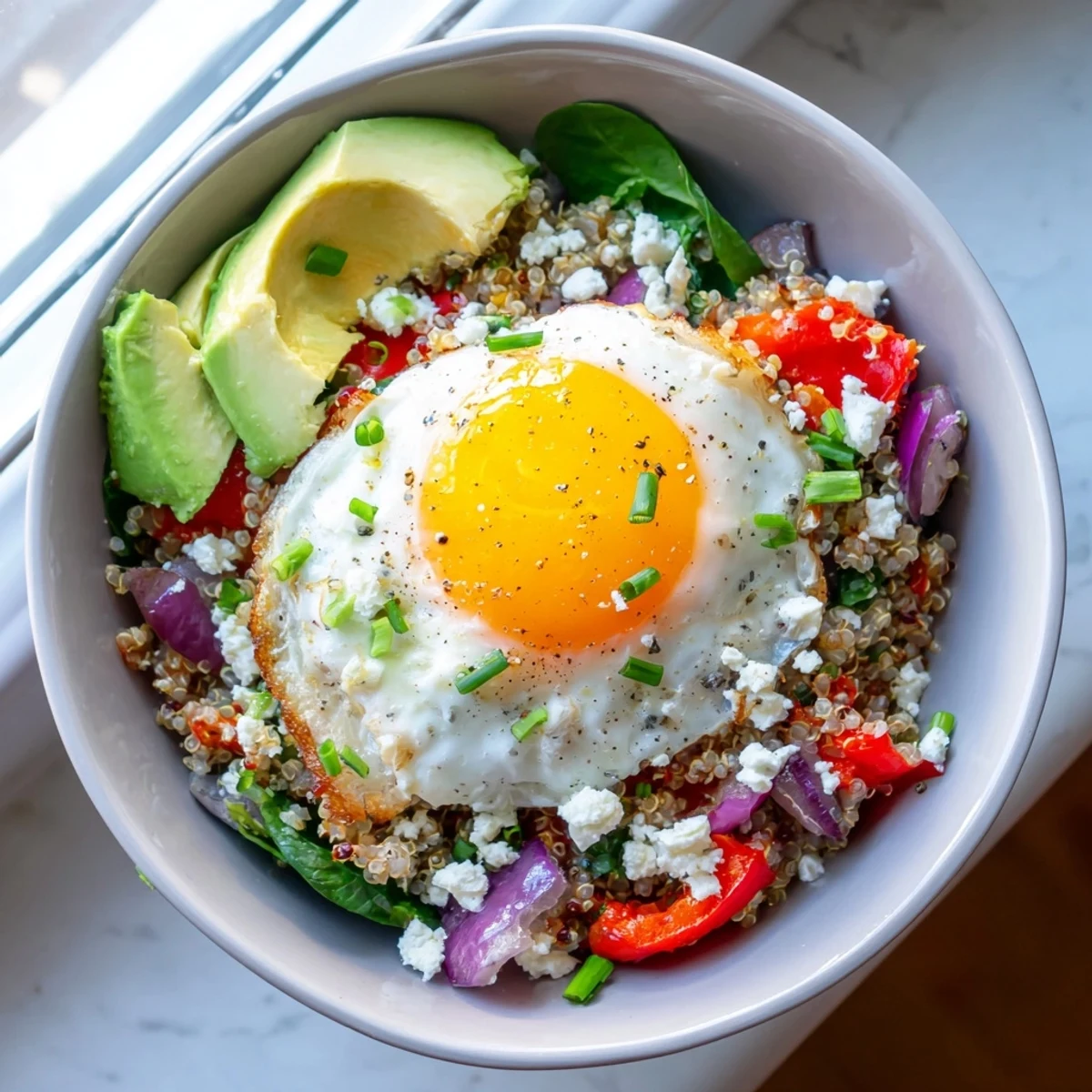 Golden fried egg resting atop fluffy quinoa breakfast bowl with colorful sautéed vegetables
