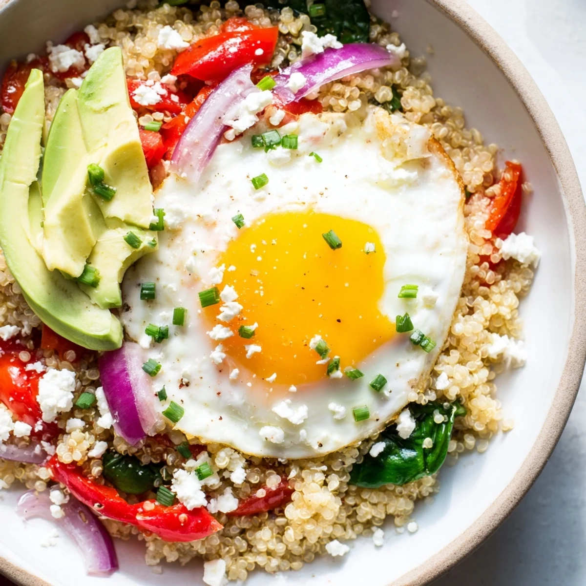 Hearty savory quinoa breakfast bowl featuring spinach, peppers, tomatoes, and perfectly cooked egg
