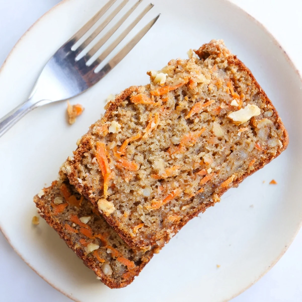 Golden spiced carrot cake banana bread slices on a wooden cutting board with scattered grated carrots