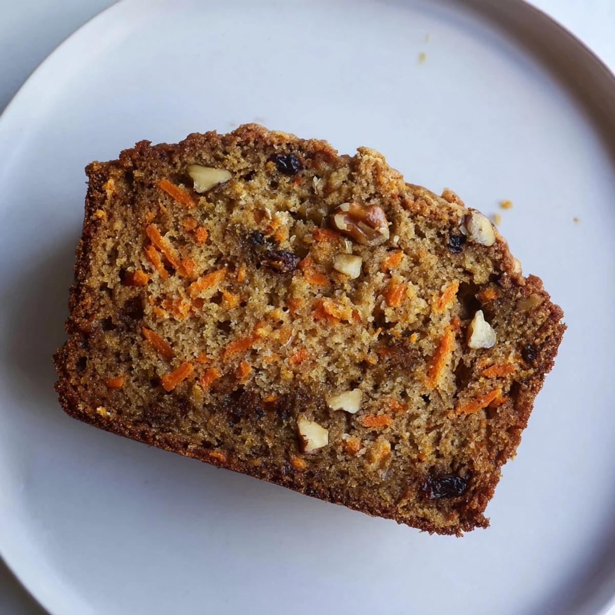 Golden carrot cake banana bread loaf sprinkled with chopped walnuts on a wooden cutting board