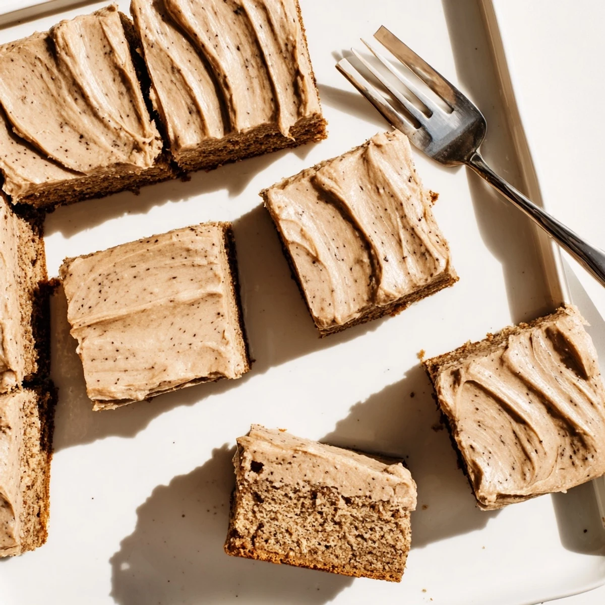 Golden frosted banana bread brownies with glossy brown butter topping on a white serving plate